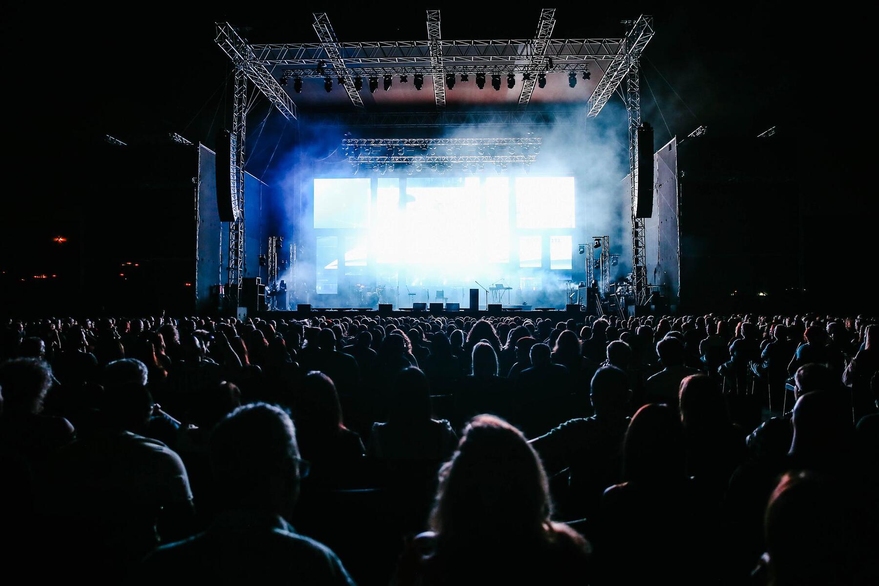 A lit stage and a dense crowd at an outdoor event after dark