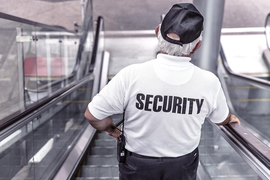 A staff member in a marked shirt seen from behind on an escalator